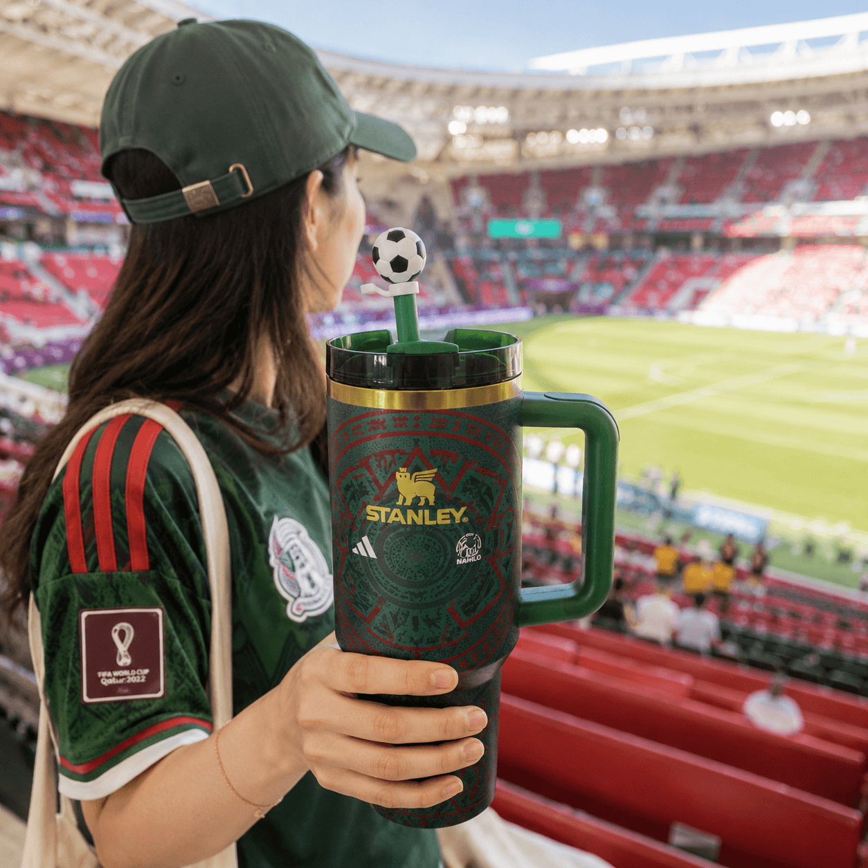 Person holding a Stanley mug with a soccer-themed design in a stadium setting