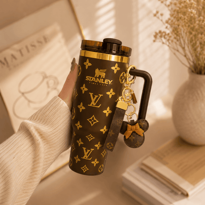 Hand holding a Stanley tumbler with Louis Vuitton monogram design, featuring a keychain.