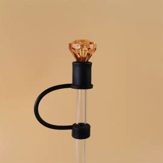 Decorative object with a clear cylindrical tube, black cap, and amber-colored top on a beige background