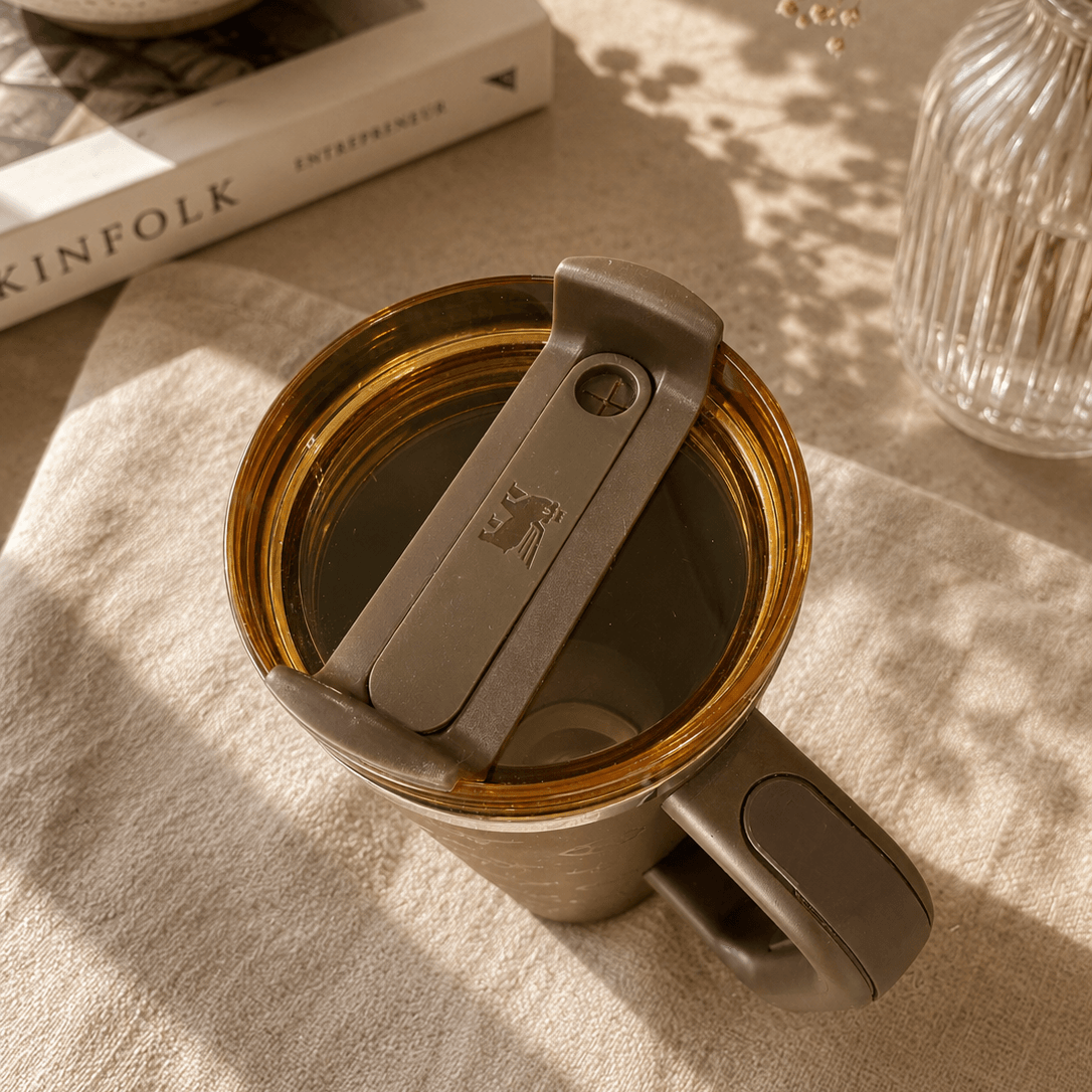 Gray mug with a lid on a textured surface with a book and decorative items in the background