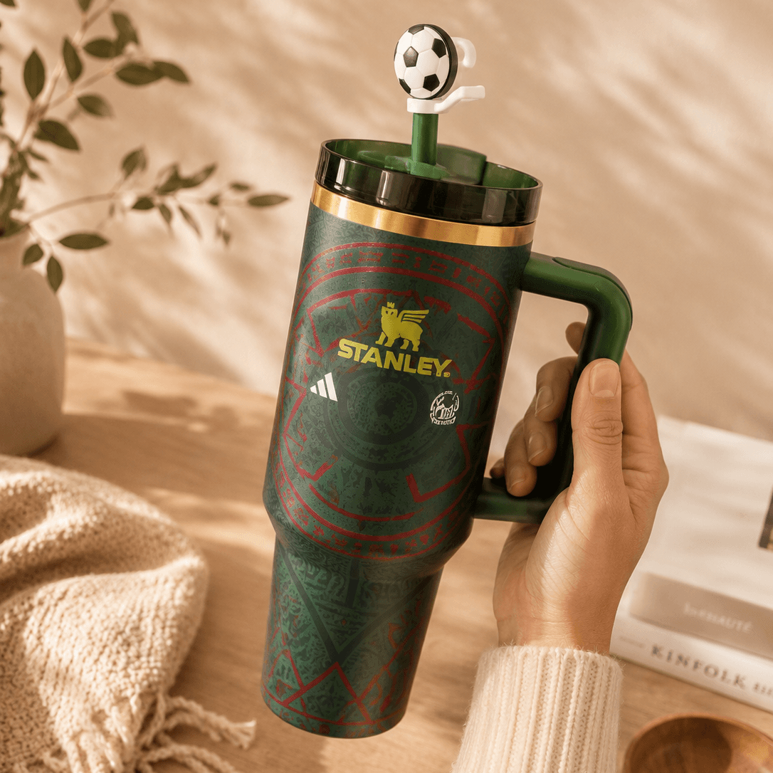 Green Stanley mug with a soccer-themed lid held by a hand on a wooden surface.