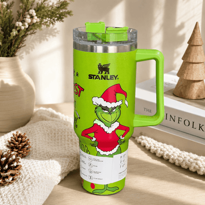 Green Stanley tumbler with Grinch design on a surface with decorative items in the background