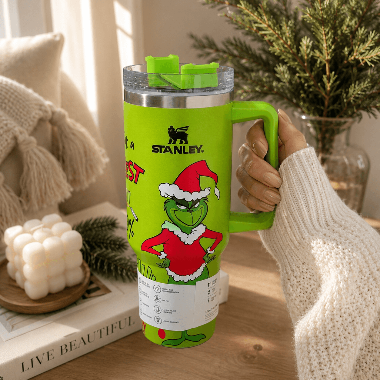 Green Stanley tumbler with Grinch design held by a person in a cozy indoor setting.