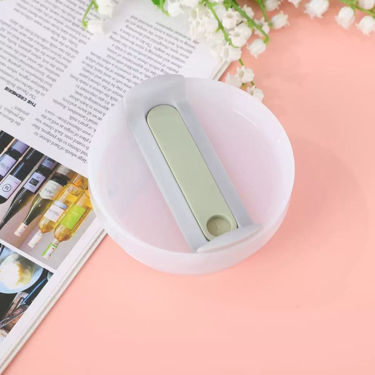Light green handheld device on a pink surface with a magazine and flowers in the background