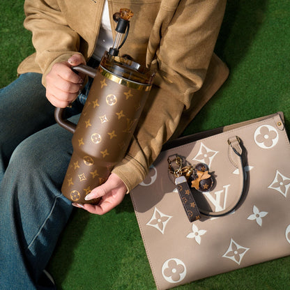 Person holding a brown patterned thermos with a matching handbag on a green surface