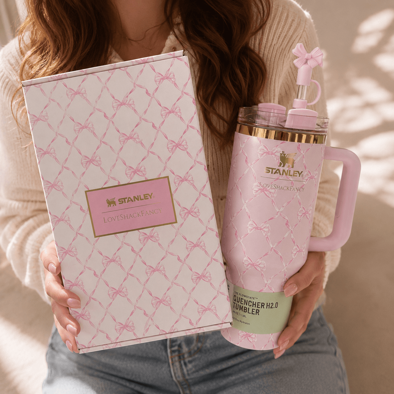 Person holding a pink Stanley tumbler and packaging with a bow design.