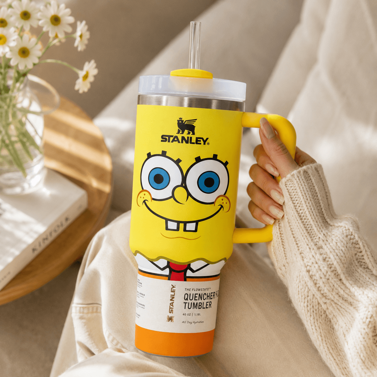 Person holding a yellow Stanley tumbler with a cartoon character design, surrounded by flowers.