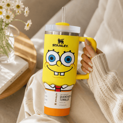 Person holding a yellow Stanley tumbler with a cartoon character design, surrounded by flowers.