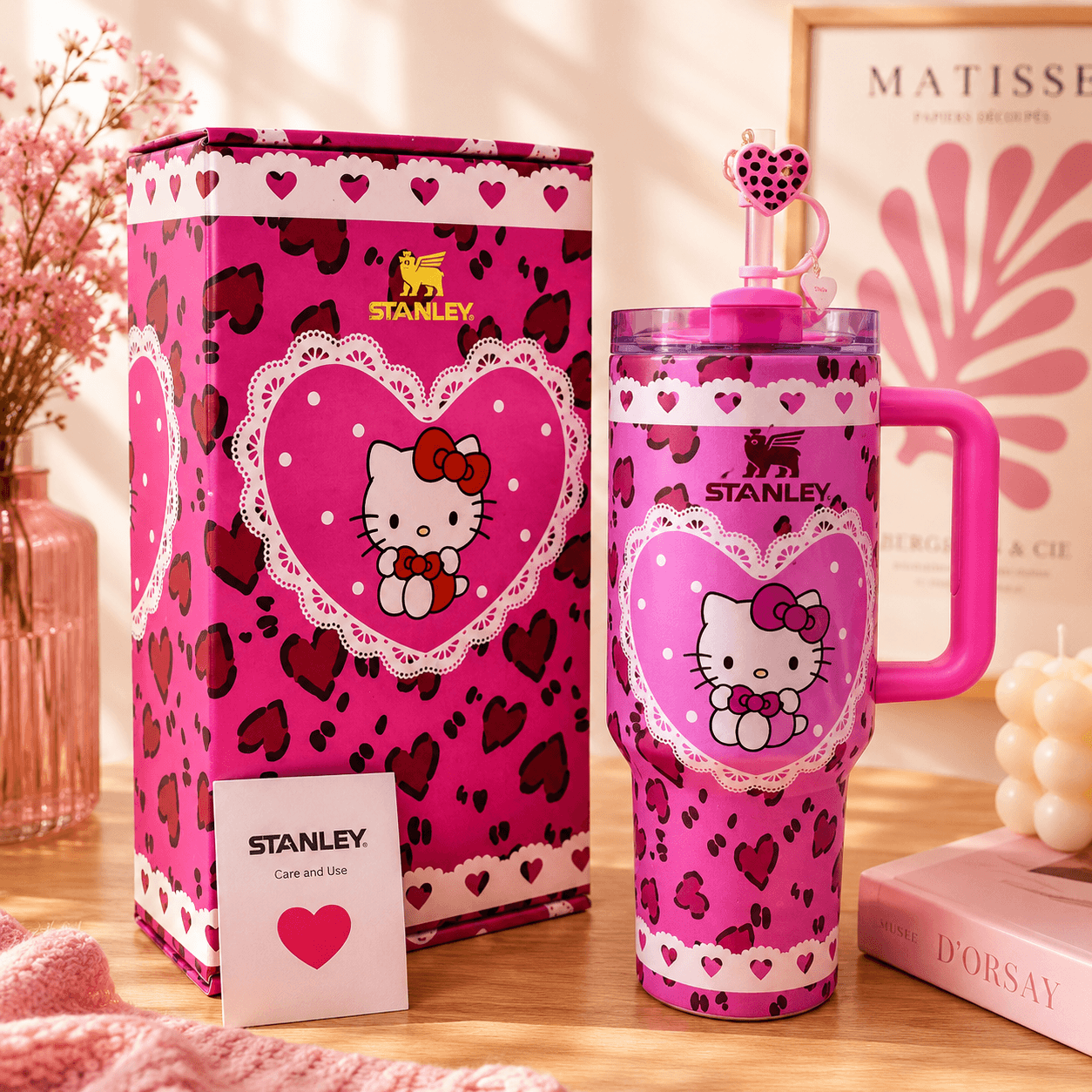 Pink Stanley tumbler with Hello Kitty design next to its packaging on a wooden surface.