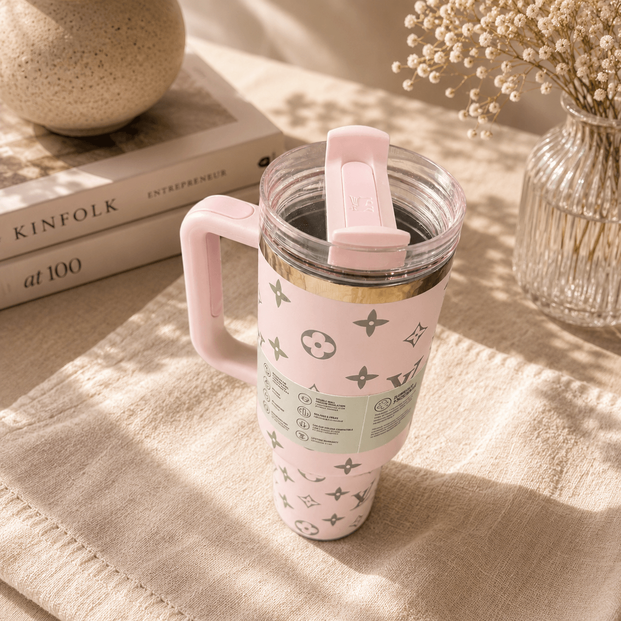 Pink travel mug with a pattern on a textured surface with books and a vase in the background