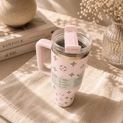 Pink travel mug with a pattern on a textured surface with books and a vase in the background