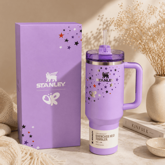 Purple Stanley tumbler with handle and stars on a beige surface with packaging and decor items.
