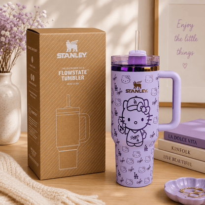 Purple Stanley tumbler with Hello Kitty design next to its packaging on a wooden surface.