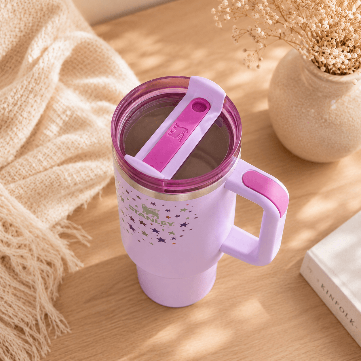 Purple travel mug with pink lid and handle on a wooden surface