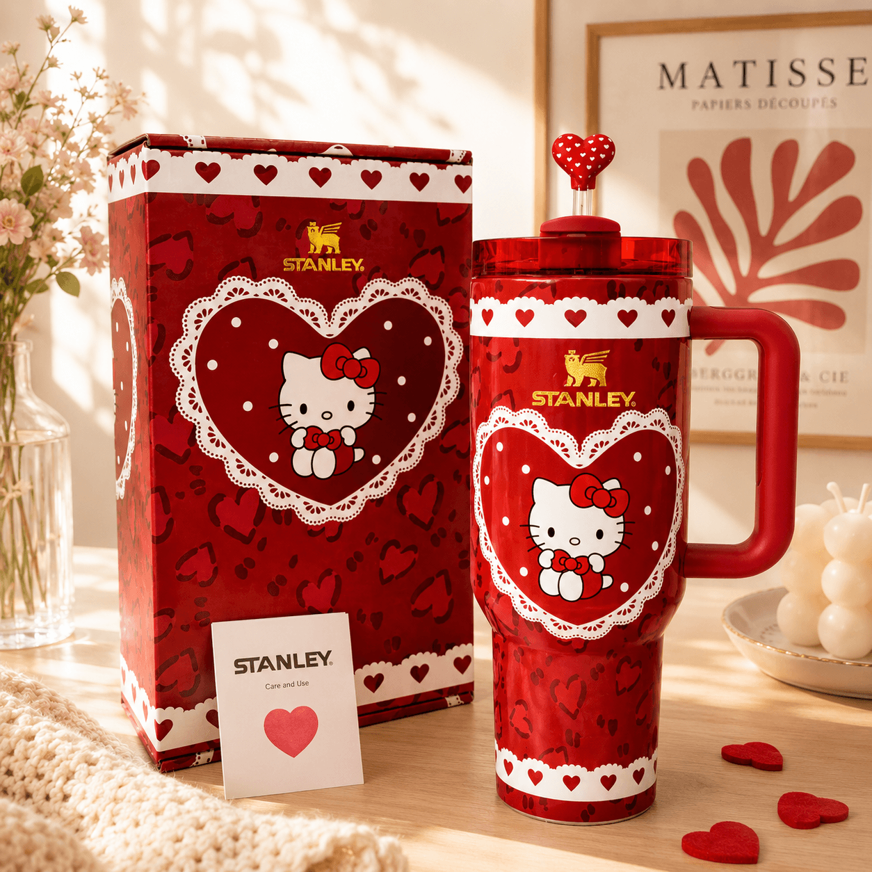 Red Stanley mug with Hello Kitty design next to its packaging on a decorative surface.