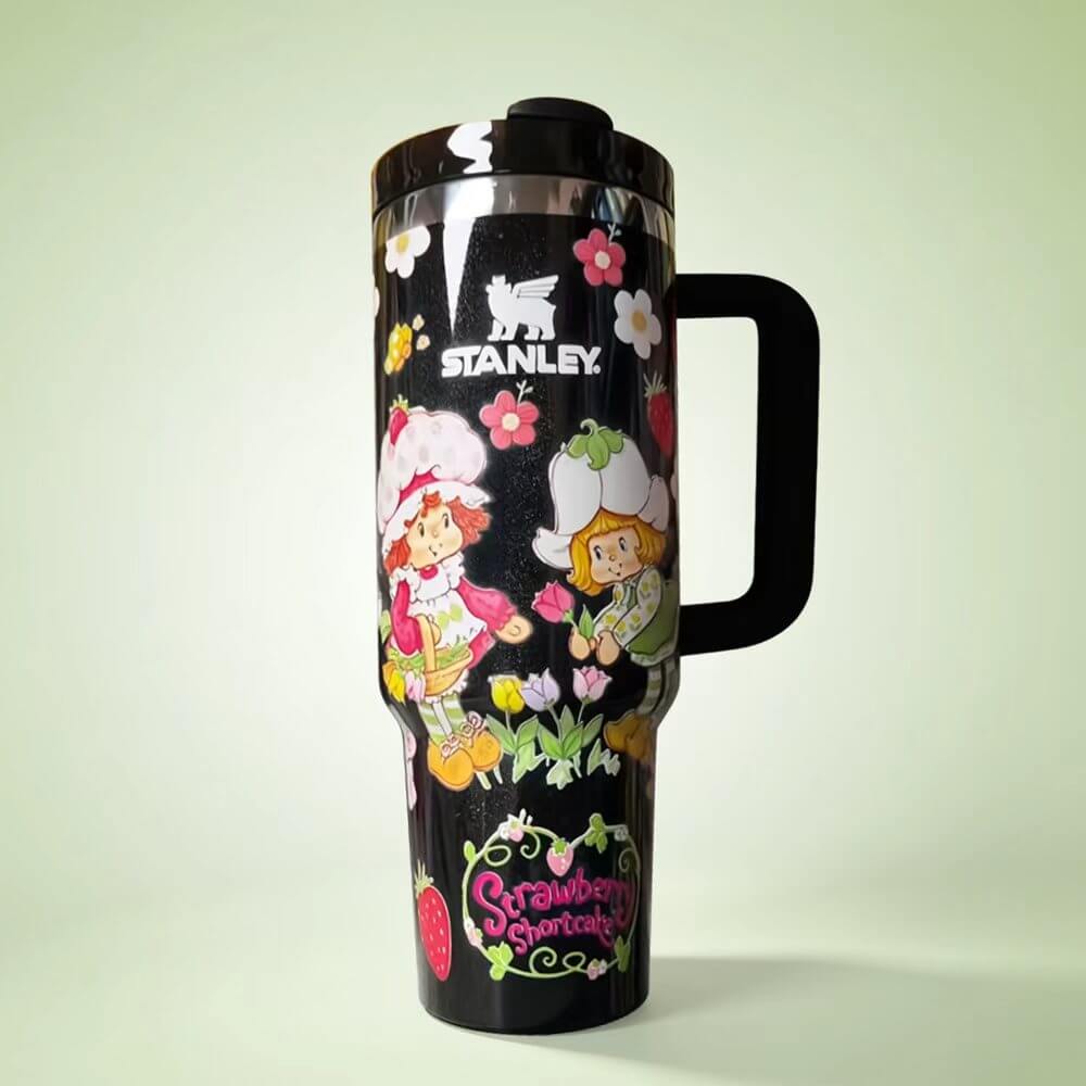 STANLEY Strawberry Garden tumbler featuring vintage strawberry-themed characters, flowers, black background, insulated construction, and ergonomic handle.