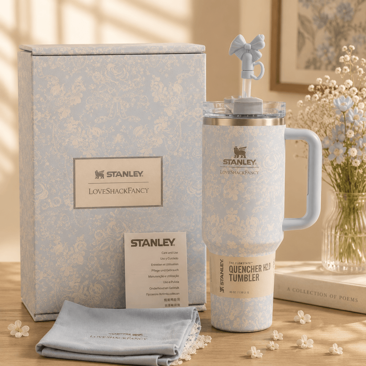 Stanley Quencher Ice Tumbler in a light blue and white damask pattern, shown with its gift box, a small towel, and a decorative lid with a bow on a wooden table.