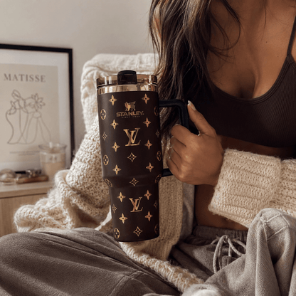 Person holding a Stanley tumbler with a Louis Vuitton pattern in a cozy indoor setting.