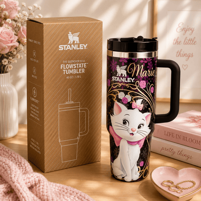 Stanley tumbler with cartoon cat design next to packaging on a wooden surface.