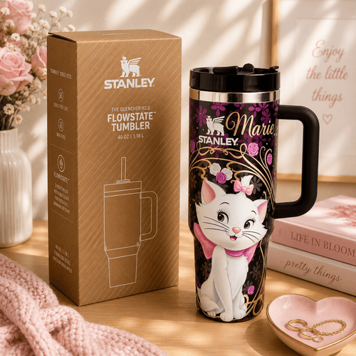 Stanley tumbler with cartoon cat design next to packaging on a wooden surface.