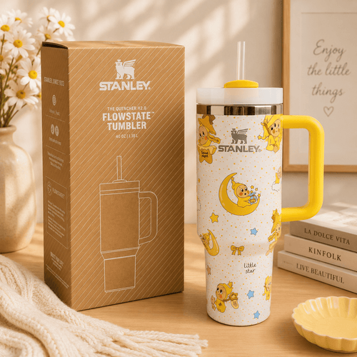 Stanley tumbler with yellow handle and cartoon design next to its packaging on a wooden surface.