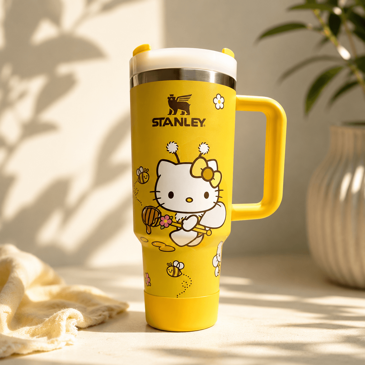 Yellow Stanley mug with Hello Kitty design on a light surface with plants in the background
