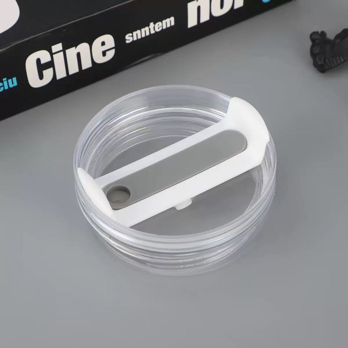 Clear plastic ring with white handle on a gray surface, with 'Cine' branding in the background.