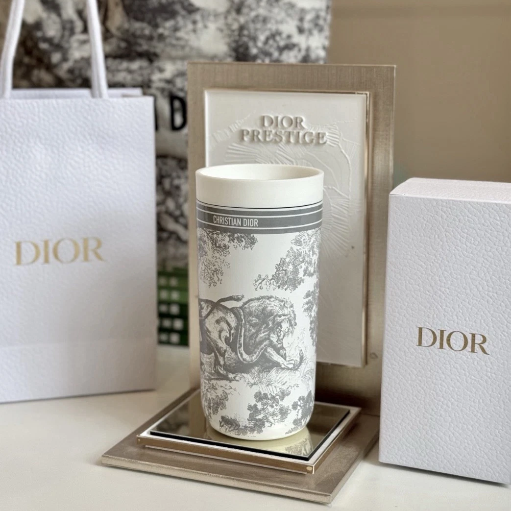 Dior Prestige ceramic cup with a grey and white toile de Jouy print, displayed on a mirrored tray with its packaging including a shopping bag, box, and card.