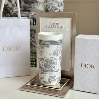 Dior Prestige ceramic cup with a grey and white toile de Jouy print, displayed on a mirrored tray with its packaging including a shopping bag, box, and card.
