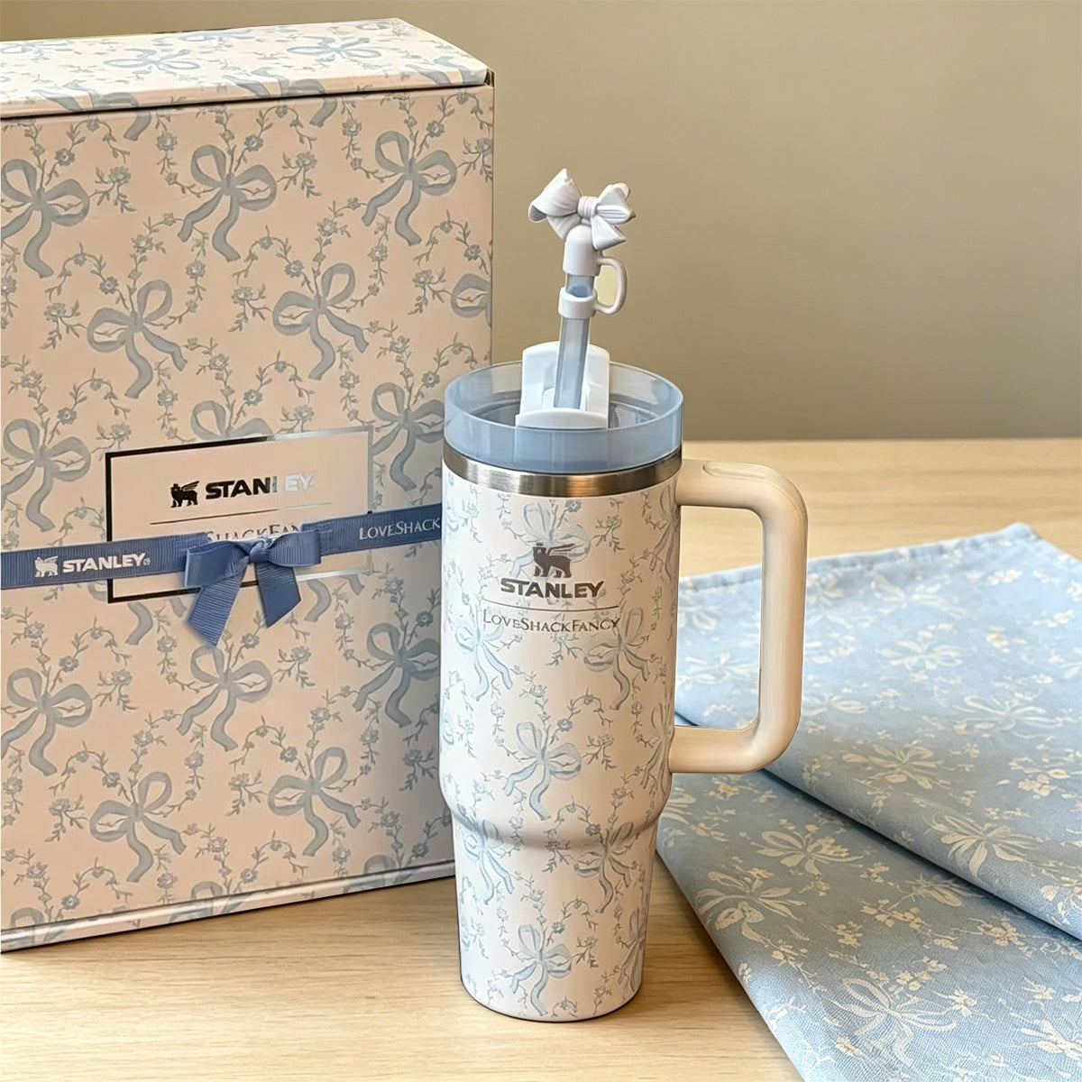 Stanley tumbler with decorative elements next to a branded box on a wooden surface.