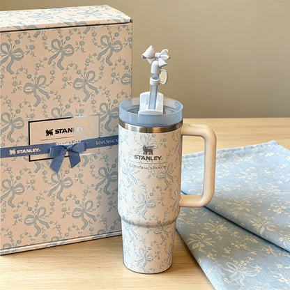 Stanley tumbler with decorative elements next to a branded box on a wooden surface.