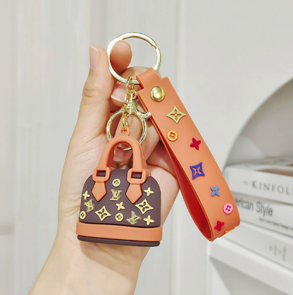 Hand holding a keychain with a small handbag design and colorful accents.